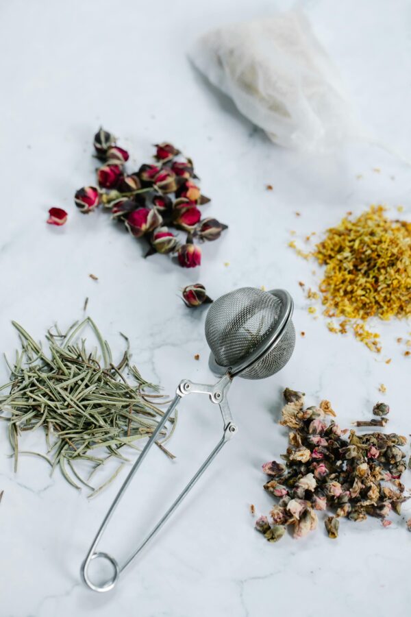 A flat lay of herbal tea ingredients with a tea strainer on a marble surface.