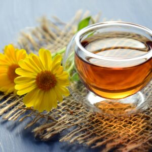 Glass cup of herbal tea with yellow flowers on a textured background.