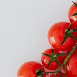 Vibrant fresh cherry tomatoes on vine with water droplets against a white background.