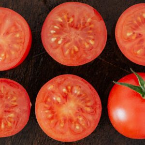 Top view closeup of fresh halves of ripe tomatoes with juice on cut side and whole tomato placed on wooden cutting board